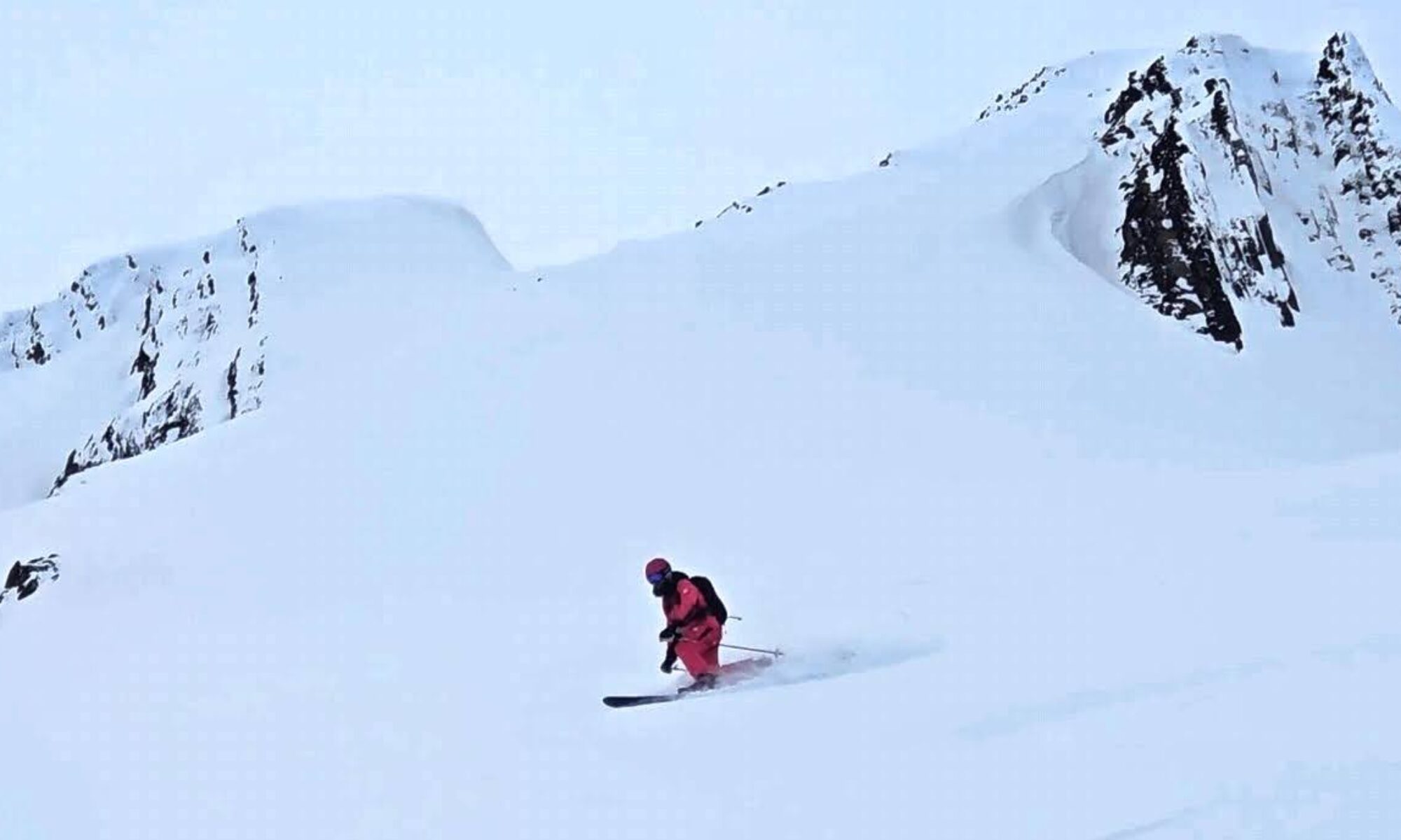 Ski instructor Colin Root telemark skiing fluffy boot-top powder in British Columbia, with jagged mountaintops in the background.